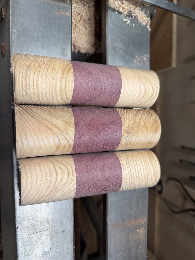 Three blanks turned to cylinders, showing the purpleheart band and the ash grain either side